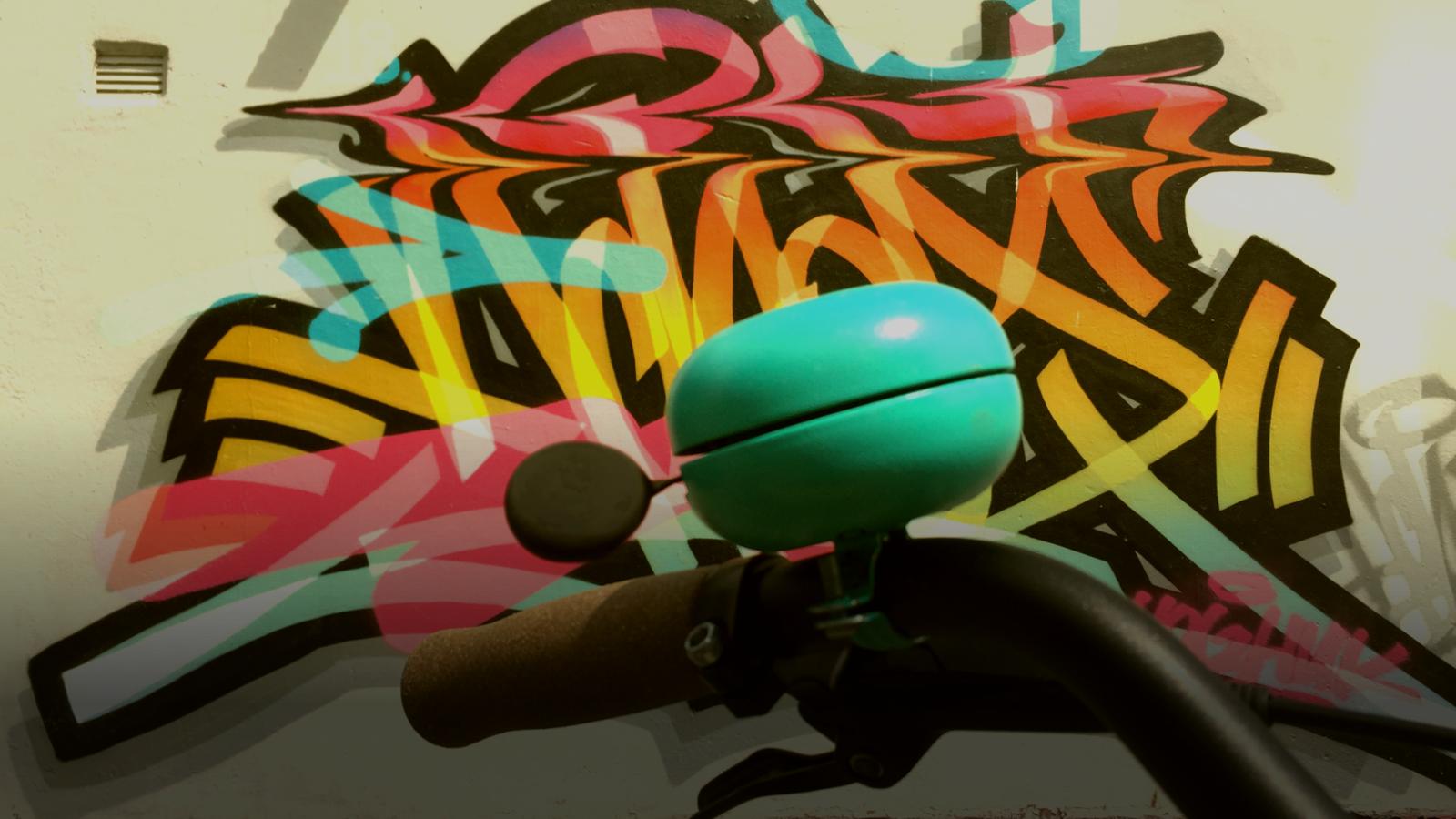 smart bicycle bell on handlebars in front of stylish graffiti