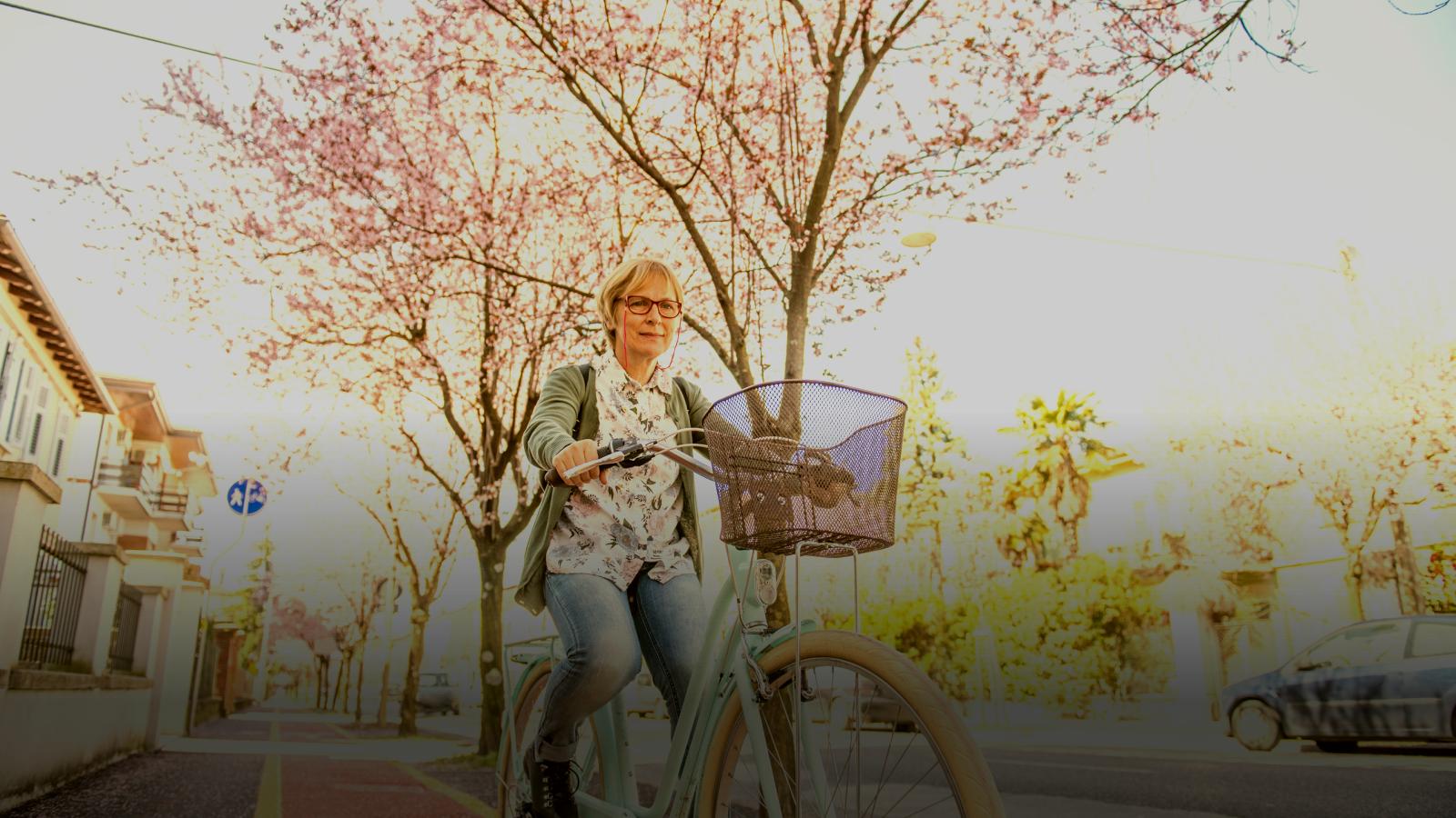 woman cycling along street with cherry blossom